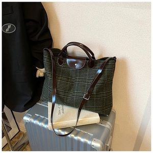 Detail of green plaid tote bag featuring brown leather straps on a vintage suitcase