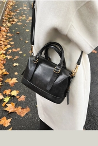 Detail of a black leather bowling bag with gold hardware against a white winter coat