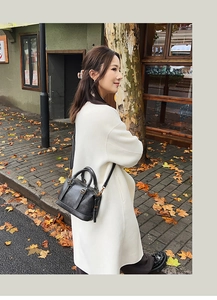 Black vintage leather bowling bag styled with a white coat on an autumn street