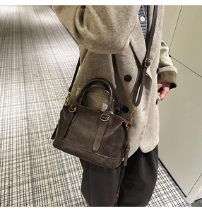 Detail shot of a dark brown leather bowling bag worn with a gray wool blazer
