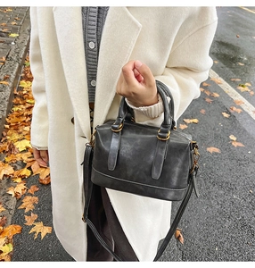 Detail of dark grey bowling bag with gold hardware held by a model in autumn scenery