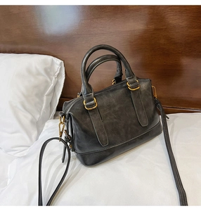 Close-up of black matte leather Boston bag with gold metal hardware on bed
