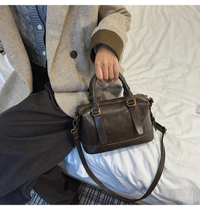 Detail of dark brown vintage bowling bag with bronze hardware on white bedding