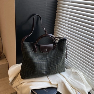 Green plaid wool tote bag with brown leather trim and long strap in sunlit shadows