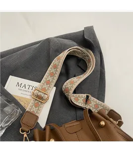 Close-up of brown textured leather bucket bag with wide geometric embroidered strap