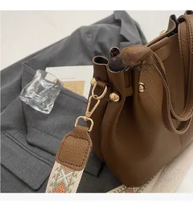 Close-up of brown litchi leather bucket bag with ethnic strap and gold hardware