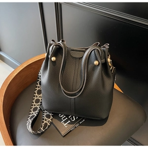 Close-up of black litchi grain leather bucket bag with geometric woven wide strap