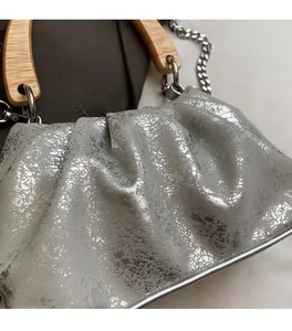 Detail of silver metallic textured pleated bag with wooden handle and silver chain strap