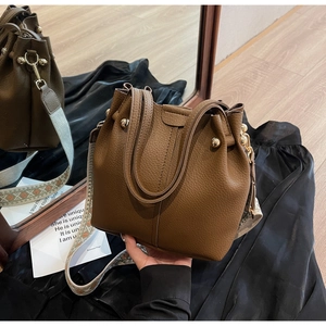 Macro detail of brown lychee leather bucket bag with wide jacquard strap and gold studs