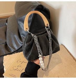 Detail of pleated black handbag featuring round wooden handle and pearl chain strap