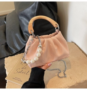 Detail of pink pleated handbag featuring large pearl chain and wooden top handle