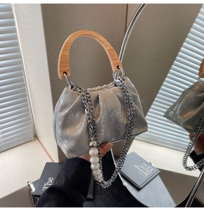 Detail of silver pleated handbag featuring a wooden handle and large pearl chain strap