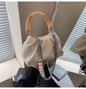 Detail of cream pleated cloud bag featuring wooden handle and pearl embellished chain