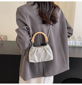 Detail of silver pleated mini bag with wooden handle and metal chain on a model