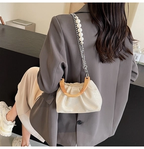 Detail of ruched white bag featuring a round wooden handle and pearl chain strap