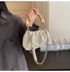 Detail of ruched beige bag featuring a wooden handle and pearl silver chain strap