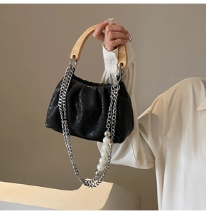 Detail of black pleated cloud bag with wooden handle and faux pearl chain strap