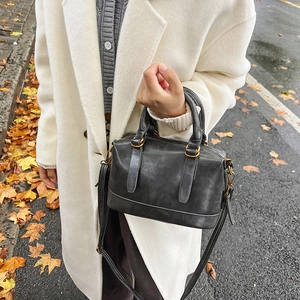 Retro black bowling handbag with gold hardware and shoulder strap in an outdoor street setting