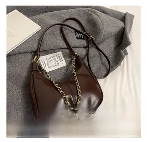 Detailed view of deep brown crescent bag with glossy leather and gold chain decoration