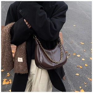 Detail of dark brown glossy leather hobo bag with gold chain and vertical stitching