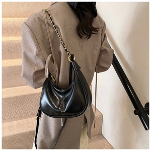 Detail of black leather crescent underarm bag with gold chain strap on a brown blazer