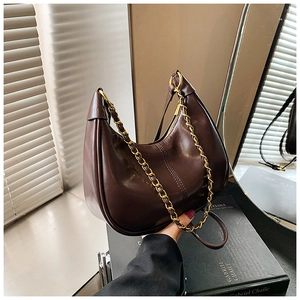 Detail of dark brown crescent underarm bag with gold chain and glossy leather texture