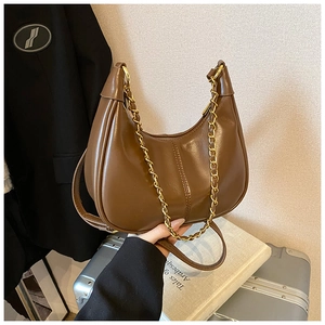 Brown faux leather crescent bag with gold chain on vintage suitcase setup