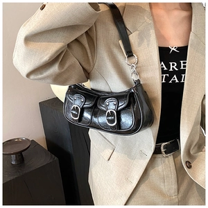 Detail of a shiny black baguette bag with silver buckles worn with a grey blazer