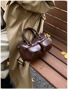 Vue détaillée du sac bowling en cuir brillant marron foncé avec poches avant sur un banc