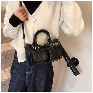 Détail d'un sac Boston en cuir verni noir porté à l'épaule avec une tenue décontractée chic
