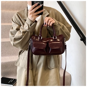 Détail d'un sac Boston bordeaux brillant avec poches avant sur un fond de manteau kaki