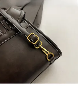 Detail of dark brown leather bag showing adjustable shoulder strap with gold metal buckle