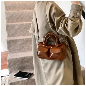 Sac Boston en cuir marron avec détails de poches porté par un mannequin en trench-coat