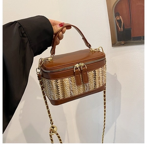 Detail of a brown leather and straw woven handbag with gold chain strap being held