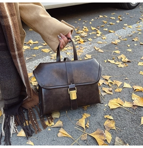 Detail of dark brown vintage faux leather bag with bronze buckle on ginkgo leaves background