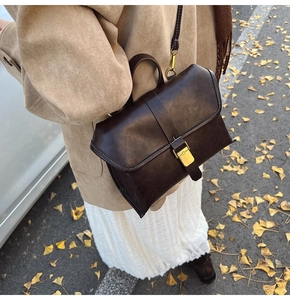 Detail of dark brown vintage leather bag with brass buckle and white stitching on autumn leaves