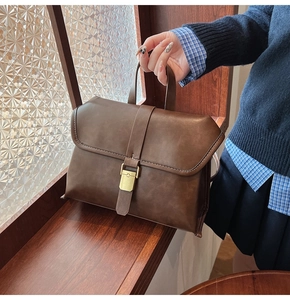 Close-up of vintage brown leather handbag with antique gold buckle and accordion sides