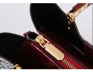 Detailed close-up of golden zipper hardware and burgundy patent leather on snakeskin bag