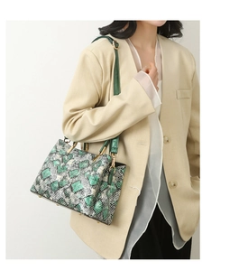 Detailed view of snake skin pattern handbag with green handles and gold metal hardware