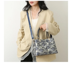 Detail of blue and grey snakeskin pattern tote with gold hardware on a beige suit model