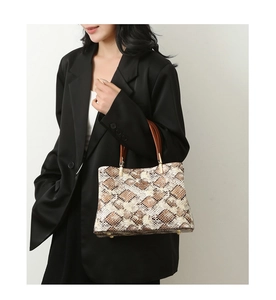 Detail of snake skin pattern handbag with brown handles and gold hardware on model