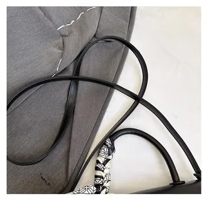Detail of black faux leather handbag strap and handle wrapped in geometric silk scarf