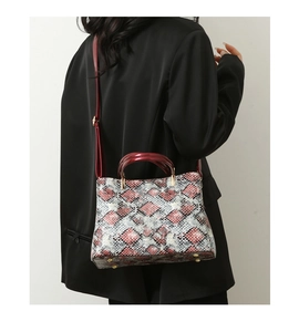 Close-up of snakeskin pattern tote with burgundy straps and gold metal feet on base