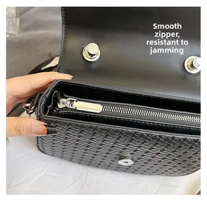 Close-up of smooth metal zipper and woven leather texture on the black crossbody bag