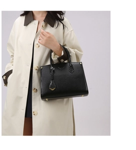 Detail of black pebbled leather handbag with triangle plaque and protective feet