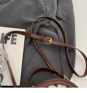 Detail view of brown leather bag with adjustable gold buckle strap and stitching