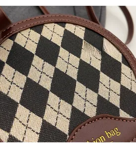 Detail of round crossbody bag featuring woven plaid fabric and leather trim with gold logo