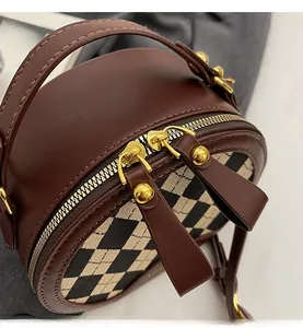 Detail of smooth gold zippers and plaid pattern on a round brown leather crossbody bag