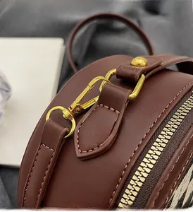 Detailed close-up of golden metal hooks and fine stitching on a brown round crossbody bag