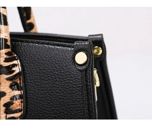Detail of black pebbled leather and leopard print pattern on luxury tote with gold rivets